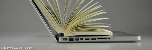 Aufgeklappter Laptop. auf dem Laptop liegt ein Buch, dessen Seiten sich auffächern. 